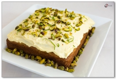 Square lime and pistachio cake on white platter decorated with lime peel and pistachios
