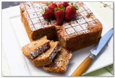 Square cake with slices and knife on white plate with strawberries on top